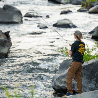 A person fishing in Deschutes River with rocks and flowing water on the banks of Riverhouse resort in Bend, Oregon.