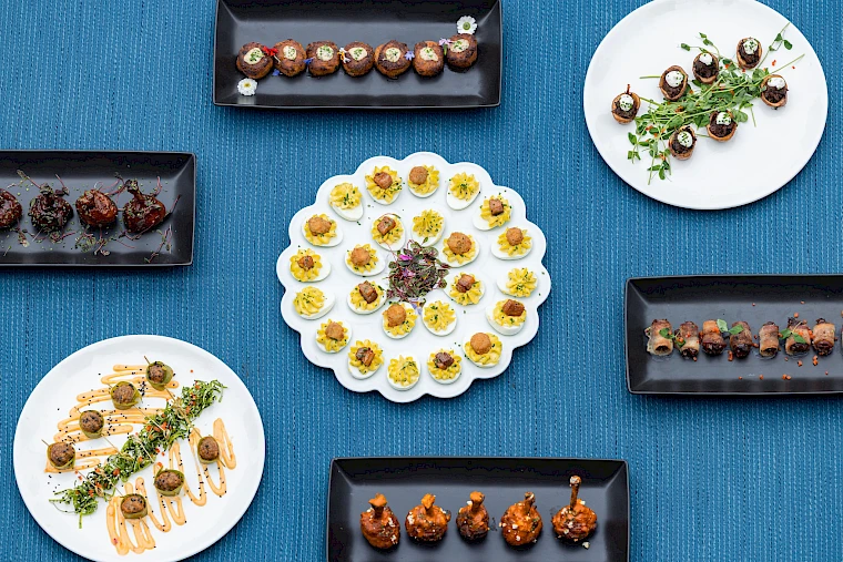 An assortment of appetizers on black and white plates arranged on a blue surface, featuring deviled eggs and various garnished finger foods.