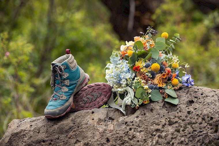 A hiking boot and a colorful bouquet rest on a rock against a blurred natural background.